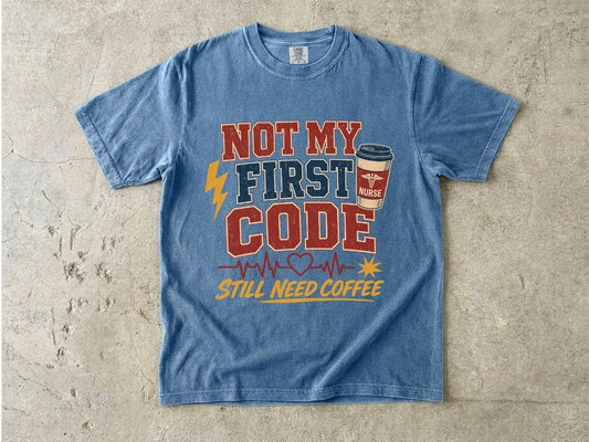 "Not My First Code, Still Need Coffee" bold retro Comfort Colors tee. Funny ER/ICU nurse gift shirt.